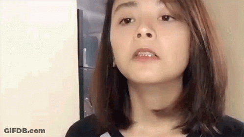 A Woman With Braces On Her Teeth Is Making A Funny Face While Standing In Front Of A Refrigerator . GIF