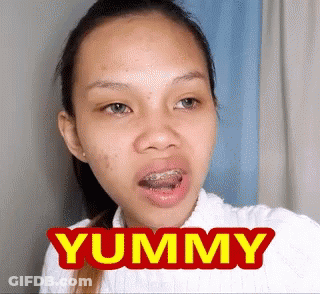 A Woman With Braces On Her Teeth Is Making A Funny Face With The Word Yummy In Front Of Her . GIF