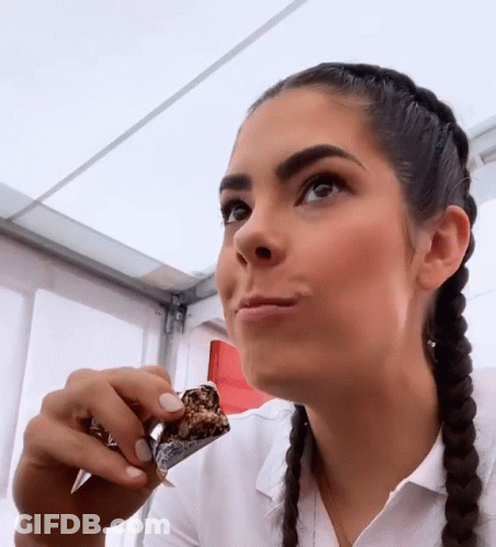 A Woman With Braids Is Eating A Piece Of Chocolate GIF