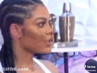 A Woman With Braids Is Sitting In Front Of A Table With Bottles Of Makeup On It . GIF