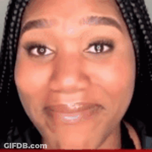 A Woman With Braids Is Smiling And Looking At The Camera . GIF