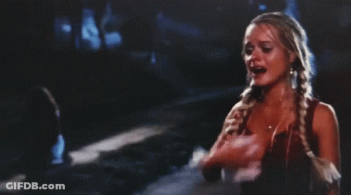 A Woman With Braids Is Standing On A Street At Night GIF