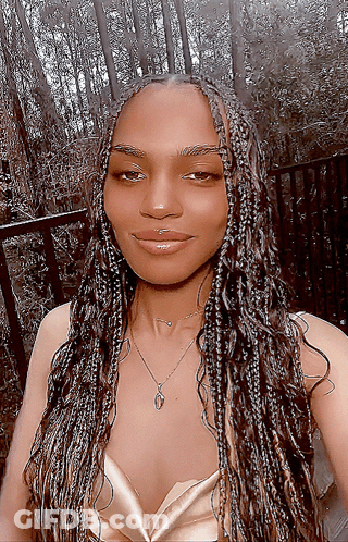 A Woman With Braids Is Wearing A Gold Top And A Necklace With The Letter O On It GIF