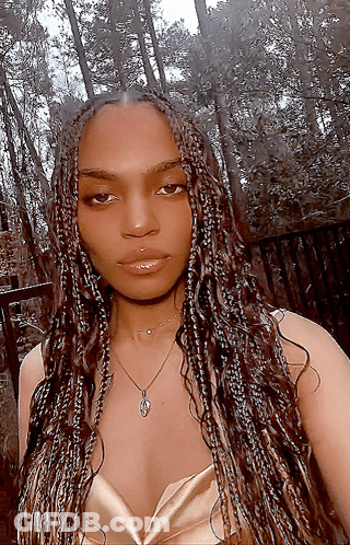A Woman With Braids Is Wearing A Necklace And A Gold Top GIF