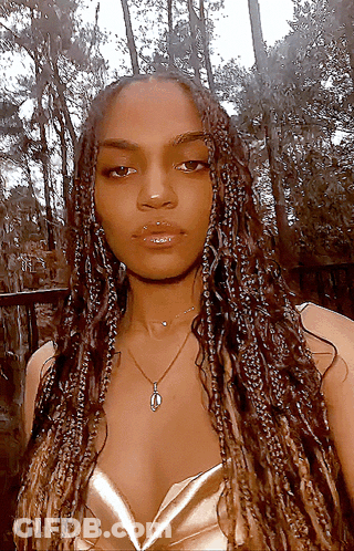 A Woman With Braids Is Wearing A Necklace And A Gold Top GIF