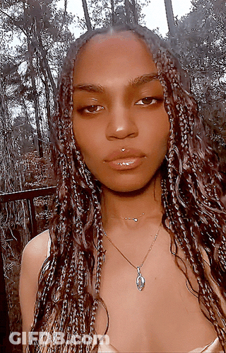 A Woman With Braids Is Wearing A Necklace With A Pendant GIF