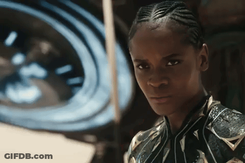 A Woman With Braids Looks At The Camera In Front Of A Large Clock GIF
