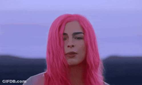 A Woman With Bright Pink Hair Is Looking At The Camera . GIF