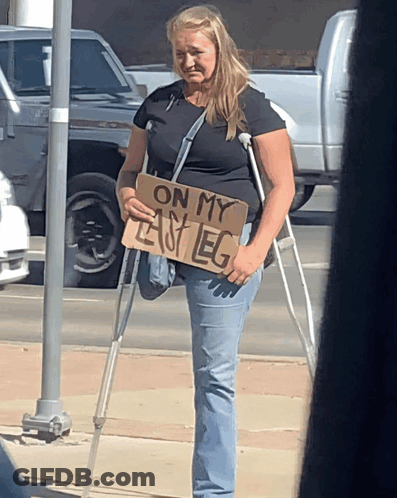 A Woman With Crutches Holding A Sign That Says On My Left Leg GIF