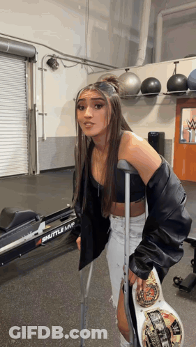 A Woman With Crutches Holds A Wrestling Championship Belt In A Gym . GIF