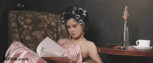 A Woman With Curlers In Her Hair Is Reading A Book GIF