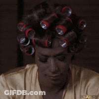 A Woman With Curlers On Her Head Is Wearing A Gold Shirt GIF