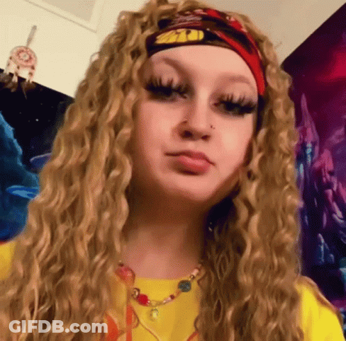 A Woman With Curly Blonde Hair Is Wearing A Headband And A Necklace . GIF