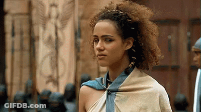 A Woman With Curly Hair And A Scarf Around Her Neck Is Standing In Front Of A Door . GIF
