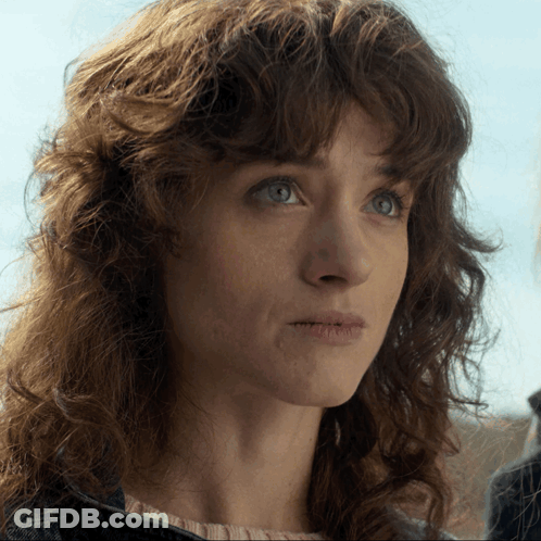 A Woman With Curly Hair And Blue Eyes Looks At The Camera GIF