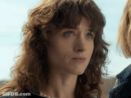 A Woman With Curly Hair And Blue Eyes Looks At The Camera GIF