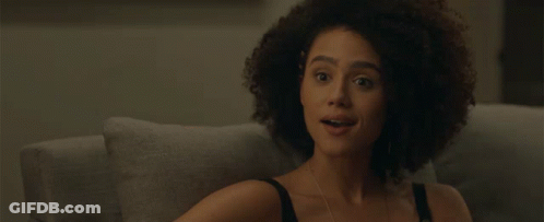 A Woman With Curly Hair Covering Her Mouth With Her Hand While Sitting On A Couch GIF