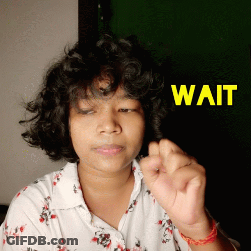 A Woman With Curly Hair Holds Her Hand Up In Front Of A Sign That Says " Wait " GIF