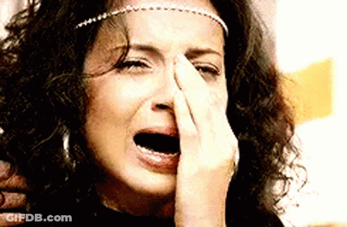 A Woman With Curly Hair Is Crying And Covering Her Nose With Her Hand GIF