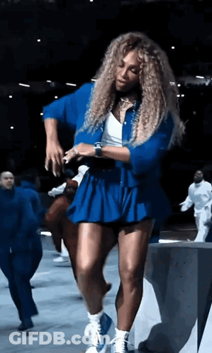 A Woman With Curly Hair Is Dancing In A Blue Dress GIF