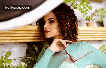 A Woman With Curly Hair Is Holding A Pair Of Glasses In Her Hand . GIF