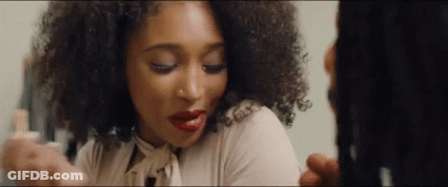 A Woman With Curly Hair Is Looking At Herself In A Mirror . GIF