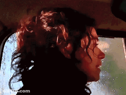 A Woman With Curly Hair Is Looking Out A Window GIF