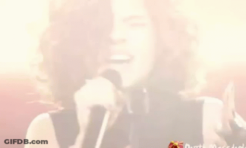 A Woman With Curly Hair Is Singing Into A Microphone While Winking . GIF
