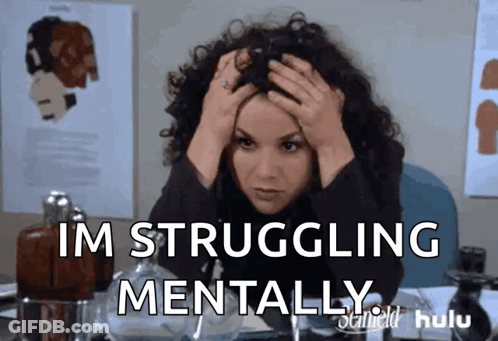 A Woman With Curly Hair Is Sitting At A Desk With Her Hands On Her Head And The Words Im Struggling Mentally GIF