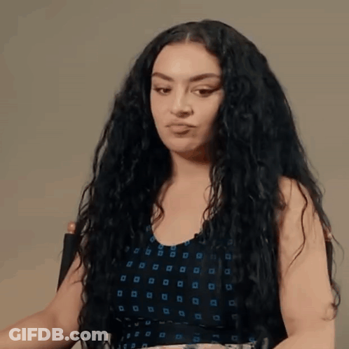 A Woman With Curly Hair Is Sitting In A Chair And Making A Funny Face . GIF