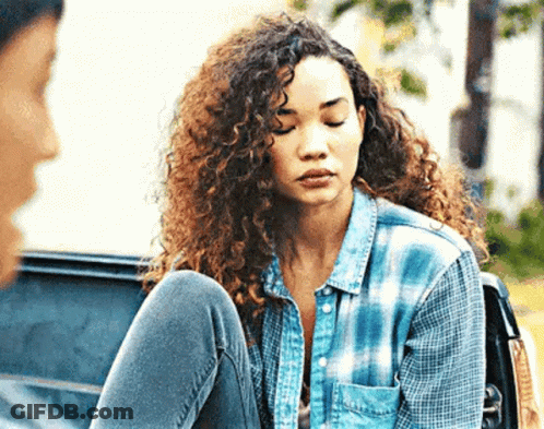 A Woman With Curly Hair Is Sitting In The Back Of A Car With Her Legs Crossed . GIF