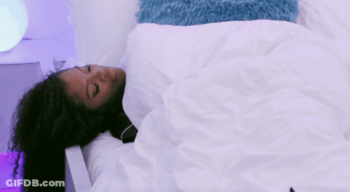 A Woman With Curly Hair Is Sleeping In A Bed With A White Blanket GIF