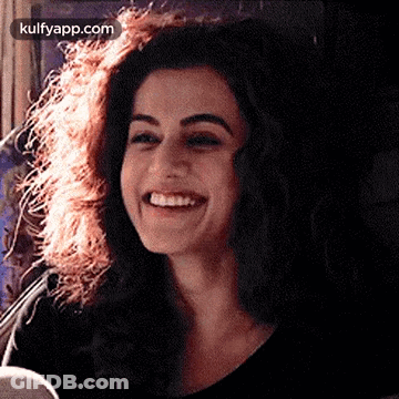 A Woman With Curly Hair Is Smiling And Wearing A Black Top . GIF