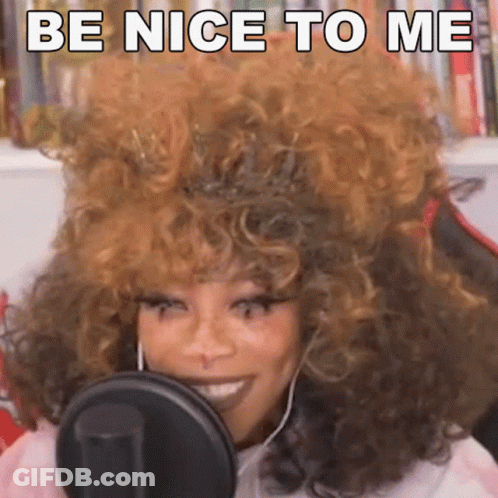 A Woman With Curly Hair Is Smiling In Front Of A Microphone And Saying Be Nice To Me GIF