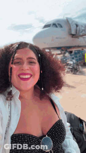 A Woman With Curly Hair Is Smiling In Front Of A Plane That Says United Airlines GIF