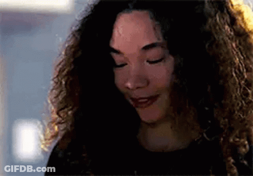 A Woman With Curly Hair Is Smiling With Her Eyes Closed And Looking Down . GIF