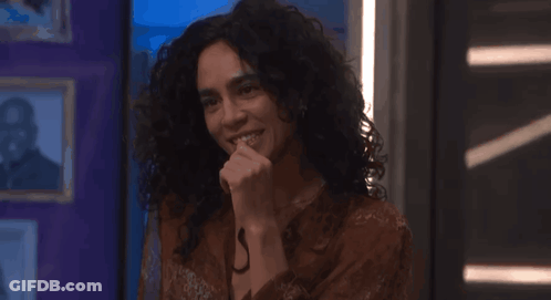 A Woman With Curly Hair Is Smiling With Her Hand To Her Mouth GIF