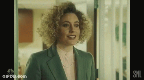 A Woman With Curly Hair Is Standing In A Doorway Wearing A Green Suit And A Pink Shirt . GIF