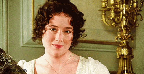 A Woman With Curly Hair Is Standing In Front Of A Candle Holder . GIF