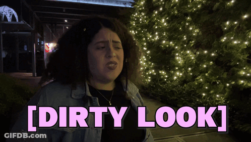 A Woman With Curly Hair Is Standing In Front Of A Christmas Tree And Says [ Dirty Look ] GIF