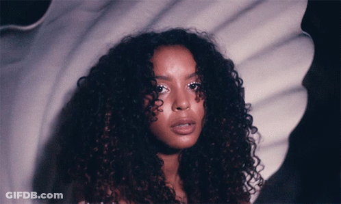 A Woman With Curly Hair Is Standing In Front Of A White Background GIF