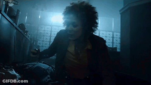 A Woman With Curly Hair Is Standing In Front Of A Window GIF
