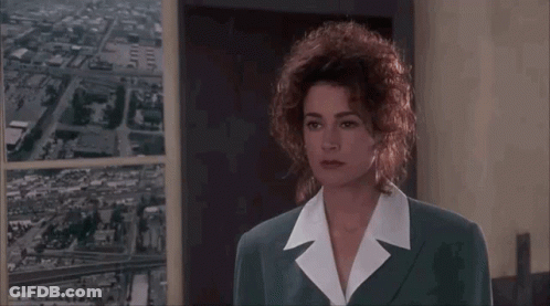 A Woman With Curly Hair Is Talking To A Man In A Suit . GIF