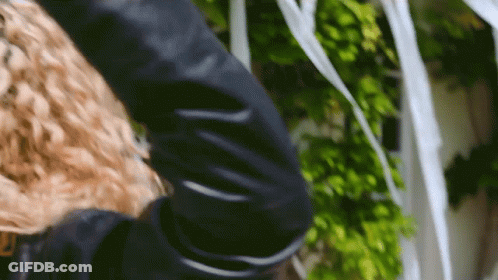 A Woman With Curly Hair Is Wearing A Black Jacket GIF
