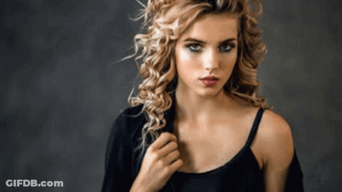 A Woman With Curly Hair Is Wearing A Black Tank Top And A Jacket . GIF