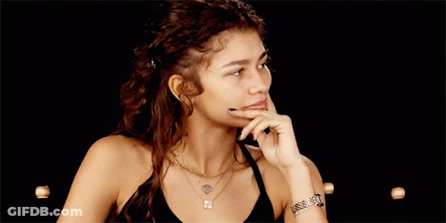 A Woman With Curly Hair Is Wearing A Black Tank Top And A Necklace With The Letter E On It GIF