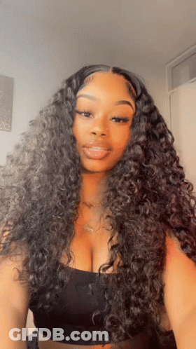 A Woman With Curly Hair Is Wearing A Black Top And A Necklace GIF
