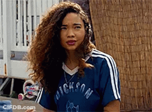 A Woman With Curly Hair Is Wearing A Blue Shirt With White Stripes And A Necklace . GIF