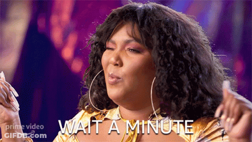 A Woman With Curly Hair Is Wearing A Gold Shirt And Earrings And Says Wait A Minute GIF