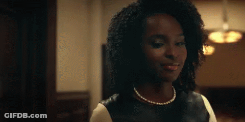 A Woman With Curly Hair Is Wearing A Pearl Necklace And A Black Leather Top . GIF